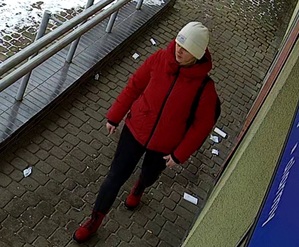zdjęcie kolorowe: kobieta w czerwonej kurtce puchowej, jasnej czapce zimowej, czarnych spodniach i czerwonych butach idąca chodnikiem