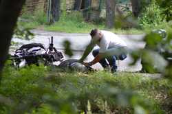 zdjęcie kolorowe: męzczyzna schylający się nad motocyklistą, który uległ wypadkowi drogowemu