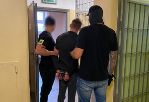 zdjęcie kolorowe: dwóch policjantów wydziału kryminalnego trzyma mężczyznę za ręce, na które załozono kajdanki.