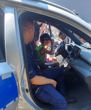 zdjęcie kolorowe: policjant siedzący w radiowozie i chłopczyk siedzący za kierownicą radiowozu