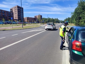 zdjęcie kolorowe: policjantka stojąca przy samochodzie osobowym na jezdni i rozmawiająca z kierujący, który jest w pojeżdzie