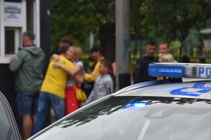 Zdjęcie kolorowe przedstawia sygnały świetlne Policji na tle kibiców.