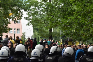 Zdjęcie kolorowe przedstawia policjantów zabezpieczających teren przed stadionem piłkarskim.