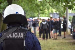 Zdjęcie kolorowe przedstawia policjanta zabezpieczającego okolice stadionu.