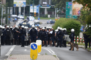 Zdjęcie kolorowe przedstawia policjantów zabezpieczających przemarsz kibiców.