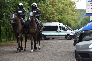 Zdjęcie kolorowe przedstawia policjantów jeźdźców koni służbowych patrolujących teren w koło stadionu piłkarskiego.