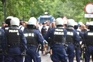 Zdjęcie kolorowe przedstawia policjantów zabezpieczających przemarsz kibiców.