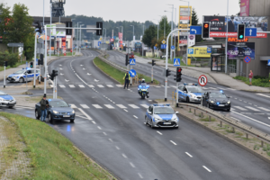 Zdjęcie kolorowe przedstawia policjantów zabezpieczających skrzyżowanie przed przemarszem kibiców.