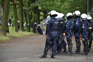 Zdjęcie kolorowe przedstawia policjantów zabezpieczających miejsce przed stadionem piłkarskim.