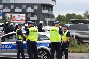 Zdjęcie kolorowe przedstawia policjantów zabezpieczających teren przyległy do stadionu piłkarskiego.