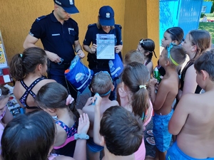 zdjęcie kolorowe: dwóch policjantów oraz grupa dzieci rozmawiających o bezpieczeństwie nad wodą