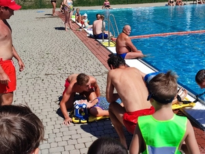 zdjęcie kolorowe: ratownicy wodni, którzy na basenie pokazują zebranym dzieciom resuscytacje osoby wymagającej pomocy