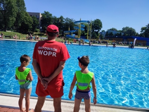 zdjęcie kolorowe: ratownik nadzorujący na basenie kąpiące się osoby w towarzystwie dwójki dzieci