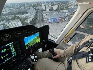 zdjęcie kolorowe: policyjny pilot w śmigłowcu patrolujący niebo nad katowickim spodkiem