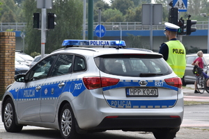 zdjęcie kolorowe: policjant ruchu drogowego stojący na skrzyżowaniu przy radiowozie