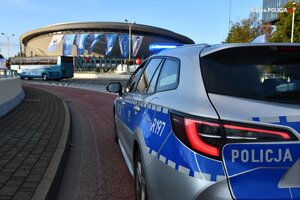 zdjęcie kolorowe: radiowóz katowickiej drogówki na tle Spodka i autokaru przewożącego zawodników na mecz siatkówki