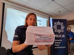 zdjęcie kolorowe:  policjantka katowickiej komendy prezentująca pokrowce profilaktyczne na  zagłówki