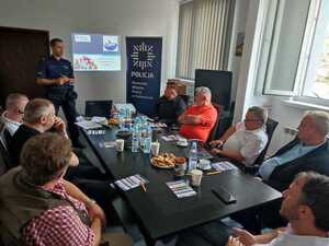 zdjęcie kolorowe: policjant katowickiej komendy z kierującymi taxi podczas spotkania profilaktycznego omawiający zasady bezpieczeństwa