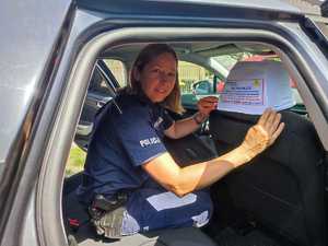 zdjęcie kolorowe: policjantka zakładająca pokrowiec profilaktyczny na zagłówek samochodowy