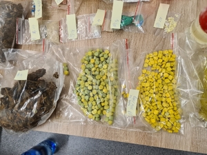 zdjęcie kolorowe: narkotyki w postaci tabletek spakowane w worki strunowe, a także zabezpieczony susz marihuany ułożone na stole