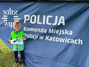 zdjęcie kolorowe: chłopczyk stojący na tle napisu Komenda Miejska Policji w Katowicach