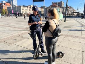 zdjęcie kolorowe: policjant rozmawiający z kobietą korzystającą z hulajnogi elektrycznej