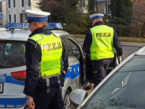 zdjęcie kolorowe: dwóch policjantów katowickiej drogówki stojących przy radiowozie