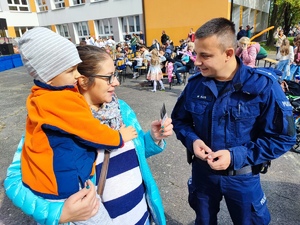zdjęcie kolorowe: dzielnicowy rozmawia z kobieta, która na rękach trzyma swoje dziecko