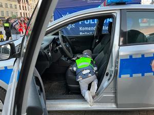 zdjęcie kolorowe: dziecko ubrane w kamizelkę odblaskowa wchodzące do policyjnego radiowozu