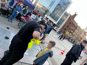 zdjęcie kolorowe: strażniczka miejska przekazująca chłopcy kamizelkę odblaskową