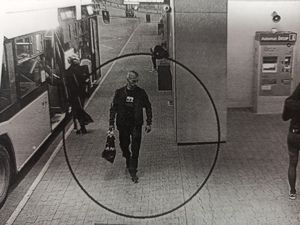zdjęcie czarno-białe: szczupły mężczyzna na peronie dworca autobusowego niosący reklamówkę w prawej ręce i plecak przewieszony przez prawie ramię
