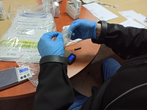 zdjęcie kolorowe: zbliżenie na ręce policjanta, który bada testerem na narkotyki czy ujawniona substancja jest narkotykiem
