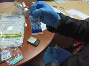 zdjęcie kolorowe: zbliżenie na dłonie policjanta trzymającego tester narkotykowy, który zabarwił się na niebiesko