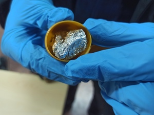zdjęcie kolorowe: plastikowe pudełko w którym ujawniono narkotyki zawinięte w folię aluminiową, trzymane przez policjanta w dłoni