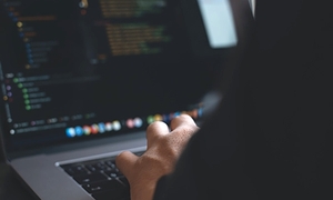 zdjęcie kolorowe: osoba siedząca przed monitorem laptopa