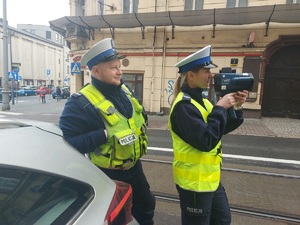 zdjęcie kolorowe: policjantka i policjant podczas wykonywania pomiaru prędkości samochodu w strefie Tempo 30