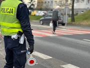 ZDJĘCIE KOLOROWE: policjant drogówki stojący przy przejściu dla pieszych, który patrzy jak przez przejście przechodzi kobieta