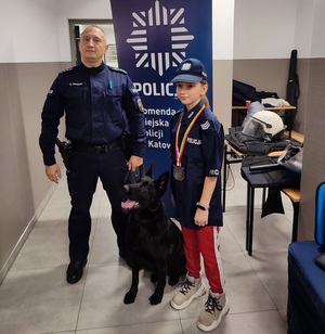 zdjęcie kolorowe: pamiątkowe zdjęcie dziewczynki z policjantem i psem służbowym