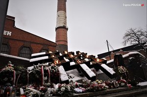 Zdjęcie kolorowe przedstawiające przedstawiające miejsce pamięci poległych górników na tle budynku Kopalni Węgla Kamiennego Wujek.