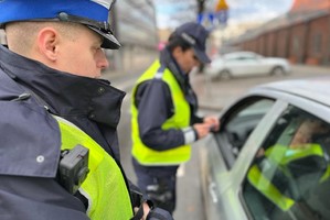 Zdjęcie kolorowe przedstawia dwóch policjantów prowadzących rozmowę z kierującym pojazdem podczas kontroli drogowej.
