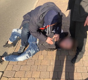 zdjęcie kolorowe:nieumundurowany policjant katowickiej komendy z zatrzymanym mężczyzną leżącym na chodniku