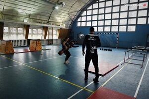 zdjęcie kolorowe: policyjny instruktor na sali gimnastycznej nadzorujący wykonywanie ćwiczeń przez kobietę