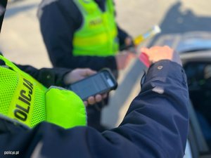 zdjęcie kolorowe:dłonie policjanta trzymającego urządzenie mobilne