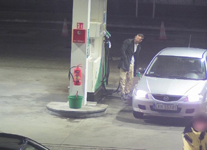 zdjęcie kolorowe: stacja paliw młody mężczyzna ubrany w piaskowe spodnie, biała koszule i ciemnoszary płaszcz i okulary korekcyjne w białych oprawkach tankujący srebrna mazdę