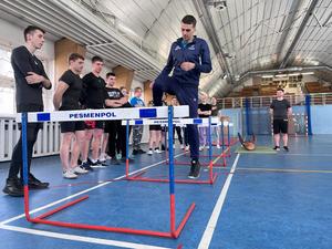 zdjęcie kolorowe: instruktor w policyjnej sali gimnastycznej pokazujący jak prawidłowo pokonać tor z płotkami lekkoatletycznymi