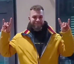 zdjęcie kolorowe:  młody mężczyzna w żółtej bluzie dresowej i czarnych dresowych spodniach unoszący ręce w gorę z dłońmi