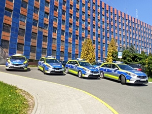 zdjęcie kolorowe: 4 oznakowane policyjne radiowozy ustawione na parkingu przed katowicką komendą