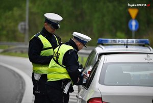 zdjęcie kolorowe: policjanci katowickiej drogówki podczas działań prędkość trzymający urządzenie do pomiaru prędkości i rozmawiający z kierującym samochodem zatrzymanym do kontroli