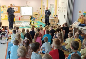 zdjęcie kolorowe: sala w przedszkolu. Dwóch Policjantów rozmawiający z dziećmi o bezpieczeństwie w ruchu drogowym