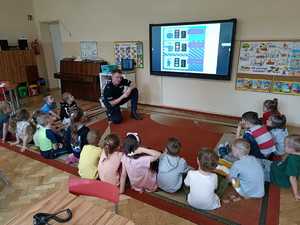 zdjęcie kolorowe: sala w przedszkolu.Policjant rozmawiający z dziećmi o  sygnalizacji świetlnej